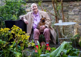  Man sitting in his garden with a small dog on his lap