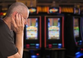A man with head in hands with poker machines in the background
